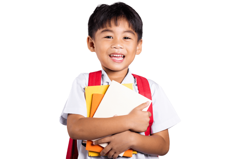 A young boy with a big smile, wearing a white shirt and red suspenders, holds a stack of colorful books. He carries a white backpack, filled with materials for his studies